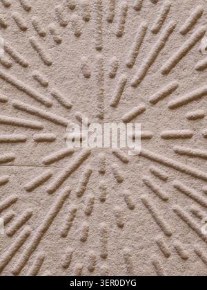 Gros plan de sable beige avec motif de rainures radiales sculptées formant un motif étoile ; un éclairage directionnel doux met en valeur la texture granulaire et les ombres Banque D'Images