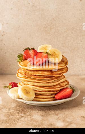 Crêpes à la banane, fraise et miel sur fond de table beige isolé. Repas du matin, petit-déjeuner d'été. Journée de crêpes ou recette de Maslenitsa Banque D'Images