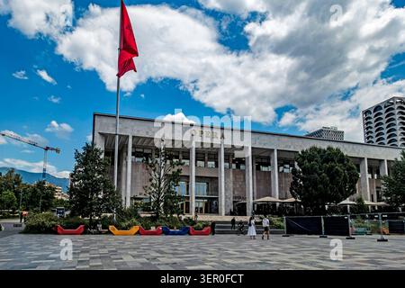 Le Palais de la culture abritant le théâtre de l'Opéra sous un ciel nuageux à Skanderbeg Square à Tirana, Albanie, avec un grand drapeau national rouge. Banque D'Images
