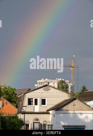 Une vue verticale saisissante d'un arc-en-ciel multicolore éclatant à travers un ciel orageux gris foncé spectaculaire au-dessus de maisons de briques de banlieue, avec un grand vous Banque D'Images