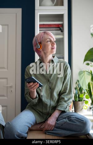 Femme mature détendue utilisant la musique en ligne à la demande plate-forme multimédia de streaming Web sur smartphone. Banque D'Images