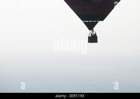 Montgolfière avec des passagers dans une nacelle silhouette contre un ciel pâle brumeux, vue aérienne minimaliste avec espace copie Banque D'Images