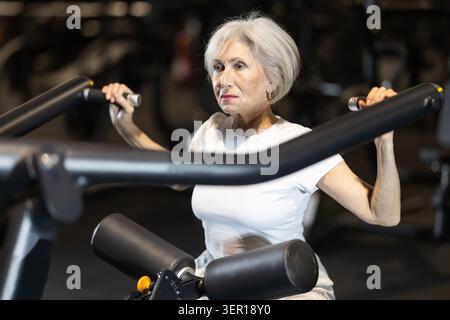 Femme âgée travaillant sur la machine de pulldown lat dans le gymnase Banque D'Images