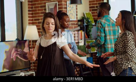 Femmes multiethniques dansant autour de la maison pendant la fête d'appartement divertissante, groupe d'amis appréciant la musique animée, faisant des mouvements de danse et buvant du vin à la réunion sociale. Banque D'Images
