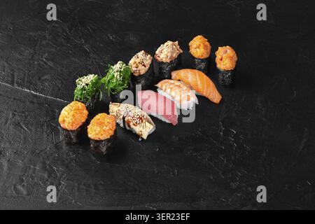 Variété de pièces de sushi disposées sur une surface texturée noire, créant une présentation élégante et appétissante Banque D'Images