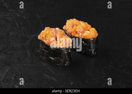 Deux délicieux morceaux de sushi Gunkan maki, remplis de thon épicé et de tobiko, sont élégamment placés sur une surface en pierre noire élégante Banque D'Images