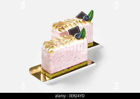 Deux tranches de délicieux gâteau meringue rose reposent sur des supports dorés, garnis de myrtilles et de chocolat Banque D'Images