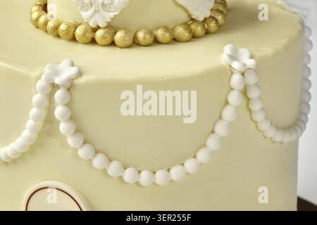 Gros plan d'un gâteau de mariage au chocolat blanc à deux niveaux, orné d'élégantes décorations de perles et de touches dorées Banque D'Images