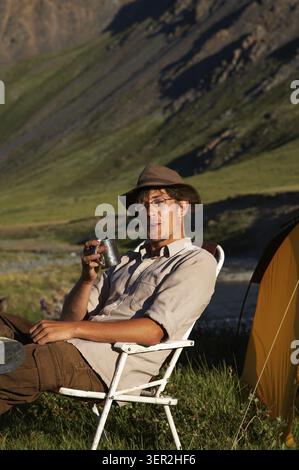 Homme assis dans la chaise au camp dans les montagnes Banque D'Images