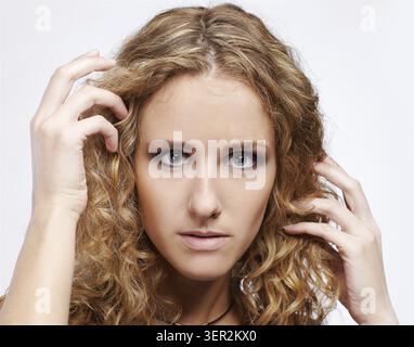 Portrait de fille blonde bouclée aux yeux bleus sur gris Banque D'Images