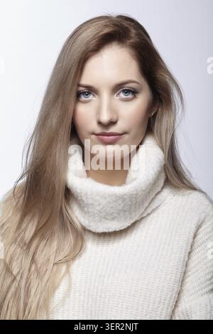 Blonde jeune belle femme vêtue d'un grand pull en laine blanche sur fond gris Banque D'Images