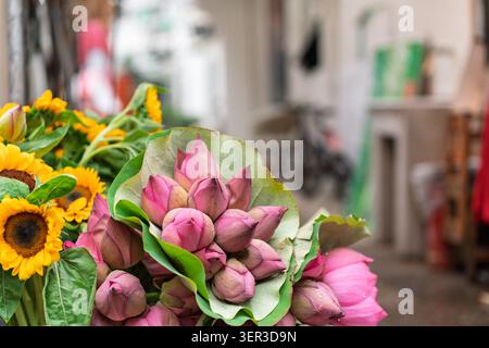 Boutons de fleurs de lotus roses (Nelumbo nucifera) enveloppés dans une feuille verte et des tournesols brillants (Helianthus annuus) exposés dans un marché de rue de Damanong, Banque D'Images