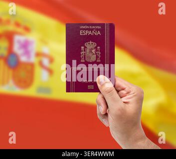 Gros plan de la main d'un homme hispanique tenant le passeport espagnol au-dessus du drapeau espagnol isolé Banque D'Images