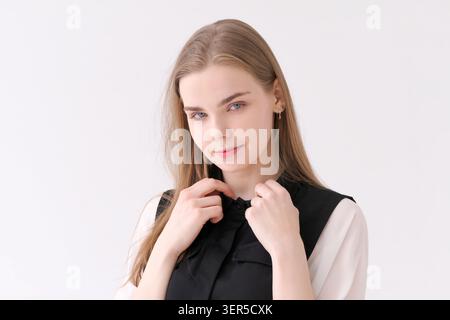 Une jeune femme blonde sympathique souriant doucement dans une combinaison noire et un chemisier blanc, un portrait de studio chaleureux et accessible Banque D'Images