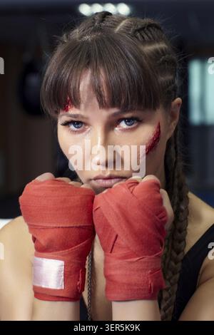 Combattant féminin avec du ruban de boxe, bandage sur ses mains se tient. La femme a une abrasion sur la joue Banque D'Images