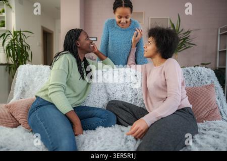 Le rire remplit l'air alors que trois amis se réunissent sur un canapé moelleux, partageant des histoires et profitant de la compagnie de l'autre. Le salon confortable rayonne de chaleur Banque D'Images