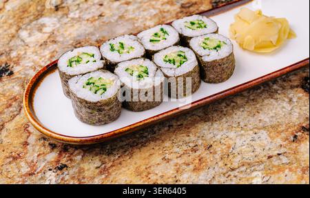 Les rouleaux de sushi au concombre fraîchement préparés sont soigneusement disposés sur une assiette blanche à côté d'une portion de gingembre mariné. Le sushi est composé de couches compactes de riz et d'algues. Banque D'Images