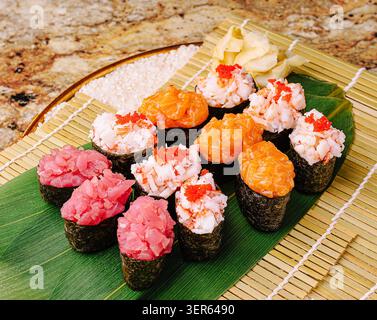 Un plateau de sushis coloré présente différents types de sushis, y compris le thon, le crabe et le saumon. Le sushi est élégamment disposé sur un tapis de bambou avec des garnitures, mettant en valeur une sélection vibrante. Banque D'Images