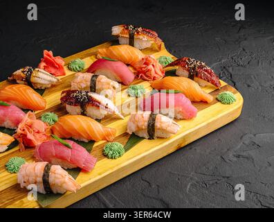 Une planche de bois présente différents types de sushis disposés soigneusement. Certaines pièces ont du poisson sur du riz, tandis que d'autres ont des garnitures colorées. Banque D'Images