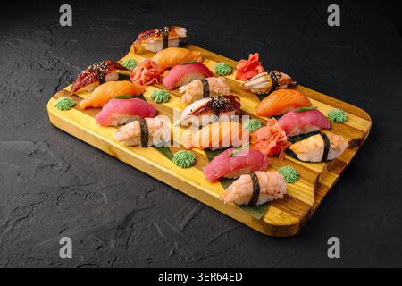 Une planche de bois présente différents types de sushis disposés soigneusement. Certaines pièces ont du poisson sur du riz, tandis que d'autres ont des garnitures colorées. Le wasabi vert et le gingembre ajoutent de la saveur. Banque D'Images