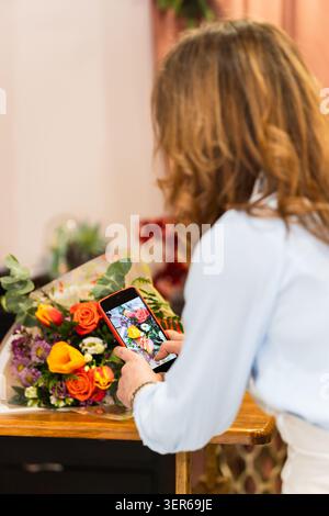 Fleuriste photographiant un bouquet coloré avec smartphone dans sa boutique de fleurs, faisant la promotion de son entreprise en ligne Banque D'Images
