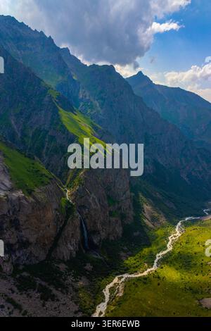 La vue aérienne capture une chaîne de montagnes accidentée avec des pentes abruptes et une herbe verte vibrante. Une rivière sinueuse coule à travers la vallée, avec un superbe w Banque D'Images