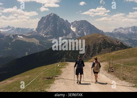 Deux randonneurs avec des sacs à dos marchant sur un chemin de terre vers les majestueux sommets alpins, trekking et concept d'aventure de voyage. Photo de haute qualité Banque D'Images