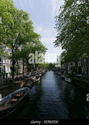 Vue verticale sur le paysage urbain d'un canal tranquille d'Amsterdam bordé d'arbres, de ponts et d'architecture traditionnelle Banque D'Images