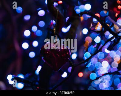 Gros plan créatif présentant une décoration en forme de coeur suspendue avec un fond lumineux flou bleu et rouge éclatant Banque D'Images