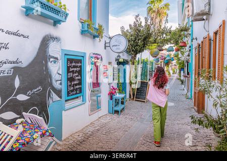 13 mai 2026, Sigacik, Turkiye : femme marchant dans une charmante rue pavée, avec une fresque murale Mustafa Kemal Ataturk et un archi méditerranéen dynamique Banque D'Images