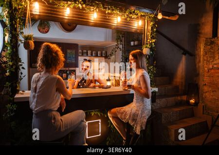 Des femmes amies appréciant des cocktails au bar animé Banque D'Images