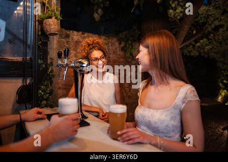 Deux jeunes femmes adultes dégustant de la bière artisanale pendant la nuit Banque D'Images