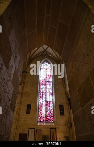 Vue sur un grand vitrail gothique aux motifs rouges et violets éclatants niché dans d'anciens murs en pierre sous un plafond voûté à Fribourg im Brei Banque D'Images