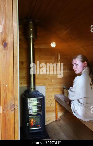 Femme détendue en peignoir debout à l'intérieur d'un sauna, embrassant un mode de vie sain, bien-être et thérapie thermale. Banque D'Images