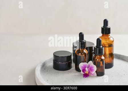 Concept naturel de soins de la peau et de soins de beauté avec des récipients cosmétiques en verre ambré disposés sur un plateau rond. Deux flacons compte-gouttes remplis de liq. Transparent Banque D'Images