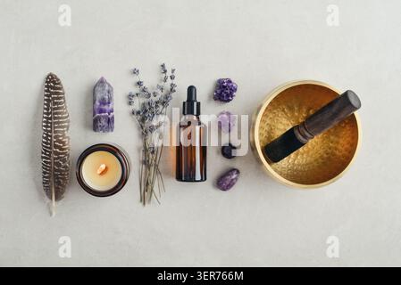 Composition de bien-être vue de dessus avec un bol chantant, un flacon compte-gouttes en verre ambré, des fleurs de lavande, des cristaux d'améthyste, des plumes et une bougie parfumée A. Banque D'Images