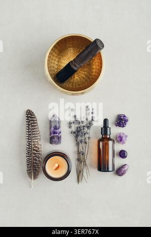 Composition de bien-être vue de dessus avec un bol chantant, un flacon compte-gouttes en verre ambré, des fleurs de lavande, des cristaux d'améthyste, des plumes et une bougie parfumée A. Banque D'Images