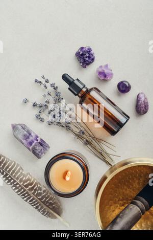 Composition de bien-être vue de dessus avec un bol chantant, un flacon compte-gouttes en verre ambré, des fleurs de lavande, des cristaux d'améthyste, des plumes et une bougie parfumée A. Banque D'Images