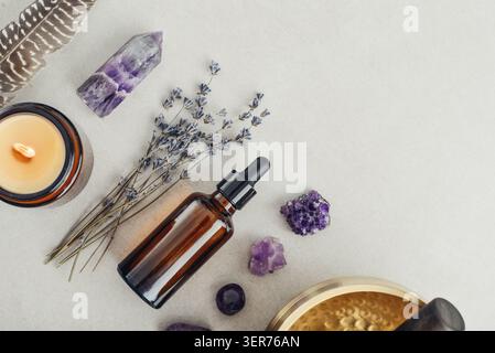 Composition de bien-être vue de dessus avec un bol chantant, un flacon compte-gouttes en verre ambré, des fleurs de lavande, des cristaux d'améthyste, des plumes et une bougie parfumée A. Banque D'Images
