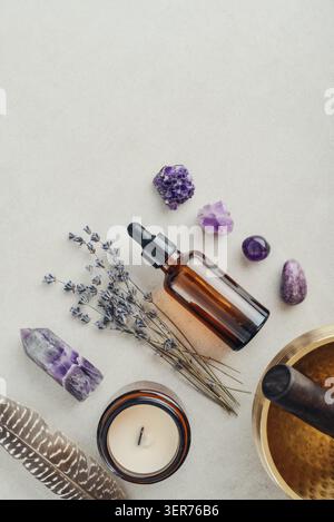 Composition de bien-être vue de dessus avec un bol chantant, un flacon compte-gouttes en verre ambré, des fleurs de lavande, des cristaux d'améthyste, des plumes et une bougie parfumée A. Banque D'Images