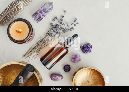 Composition de bien-être vue de dessus avec un bol chantant, un flacon compte-gouttes en verre ambré, des fleurs de lavande, des cristaux d'améthyste, des plumes et une bougie parfumée A. Banque D'Images