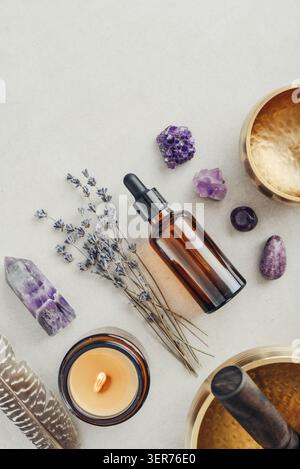 Composition de bien-être vue de dessus avec un bol chantant, un flacon compte-gouttes en verre ambré, des fleurs de lavande, des cristaux d'améthyste, des plumes et une bougie parfumée A. Banque D'Images