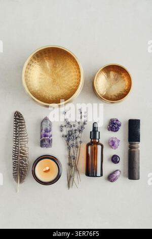 Composition de bien-être vue de dessus avec un bol chantant, un flacon compte-gouttes en verre ambré, des fleurs de lavande, des cristaux d'améthyste, des plumes et une bougie parfumée A. Banque D'Images