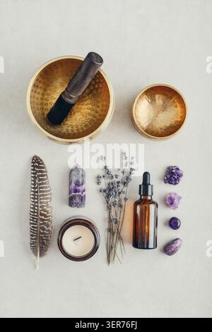 Composition de bien-être vue de dessus avec un bol chantant, un flacon compte-gouttes en verre ambré, des fleurs de lavande, des cristaux d'améthyste, des plumes et une bougie parfumée A. Banque D'Images