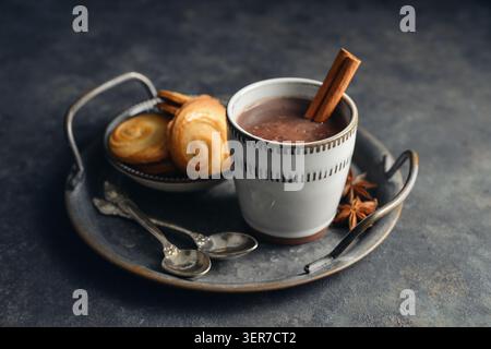 Boisson chaude traditionnelle mexicaine champurrado dans une tasse sur un plateau en métal vintage avec des biscuits, bâton de cannelle et anis étoilé sur un fond sombre. Concept Banque D'Images