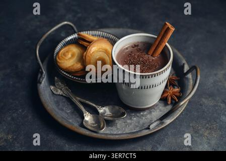 Boisson chaude traditionnelle mexicaine champurrado dans une tasse sur un plateau en métal vintage avec des biscuits, bâton de cannelle et anis étoilé sur un fond sombre. Concept Banque D'Images