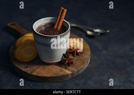 Boisson chaude traditionnelle mexicaine champurrado dans une tasse sur un plateau en métal vintage avec des biscuits, bâton de cannelle et anis étoilé sur un fond sombre. Concept Banque D'Images
