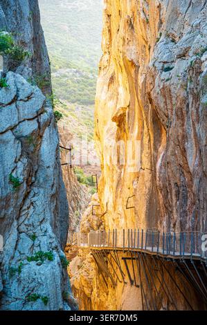 Canyon étroit avec la passerelle métallique surélevée de Caminito del Rey longeant des falaises rocheuses abruptes à Malaga, Andalousie, Espagne. Murs en pierre éclairés par le soleil et Banque D'Images
