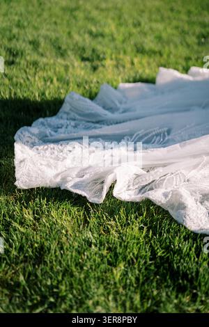 Train de robe de mariée en dentelle blanche délicate sur l'herbe verte Banque D'Images