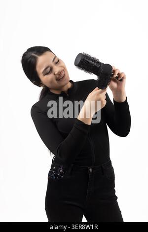 Jeune femme joyeuse séchant ses cheveux avec un sèche-cheveux noir souriant Banque D'Images